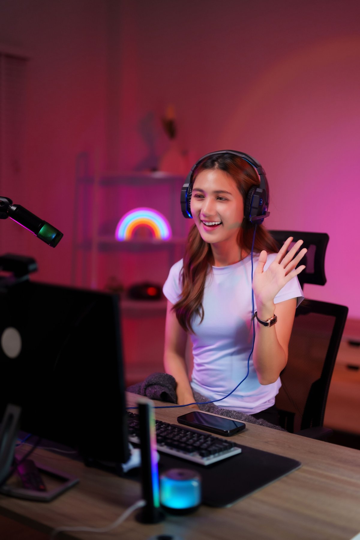 Happy content creator streaming online in a colorful room wearing a headset and greeting viewers during a broadcast